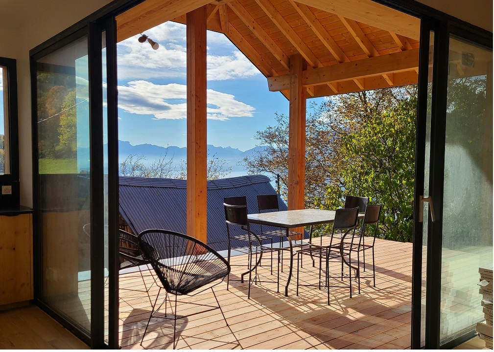 Un terrasse en bois, une table des chaises, une vue sur les montagnes et le lac