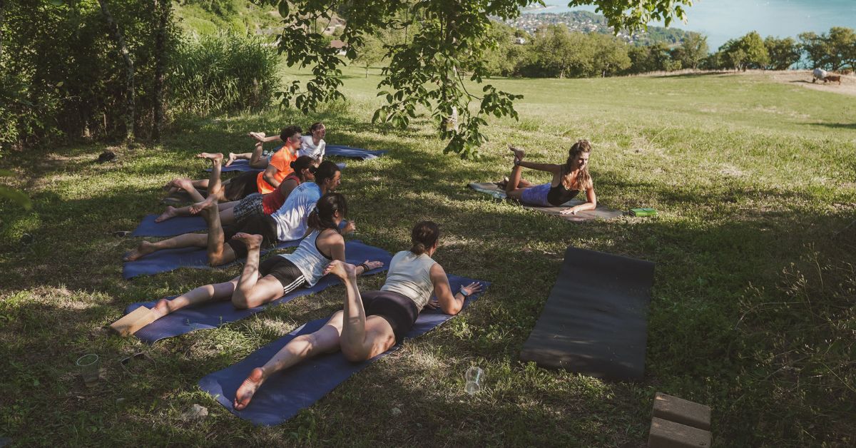 Un groupe de pratiquants participent à une séance de Yoga à L'Alpage, en extérieur, devant la vue sur le lac du Bourget.