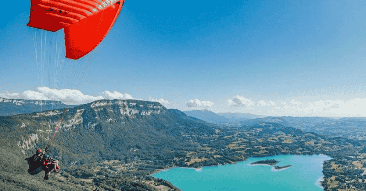 vol-parapente-annecy-les-granges-de-capucine Un parapente biplace vole au dessus du lac d'Annecy avec une voile rouge, pendant leur séjour aux gites Les Granges de Capucine.