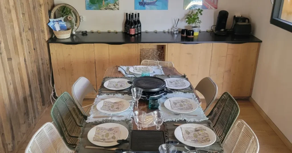 Une table est dressée pour 10 personnes dans une salle à manger moderne et chaleureuse. La table attend les participants à un séminaire au vert chez Les Granges de Capucine.